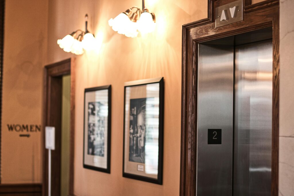 A chic interior featuring an elevator, framed art, and classic wall lighting.