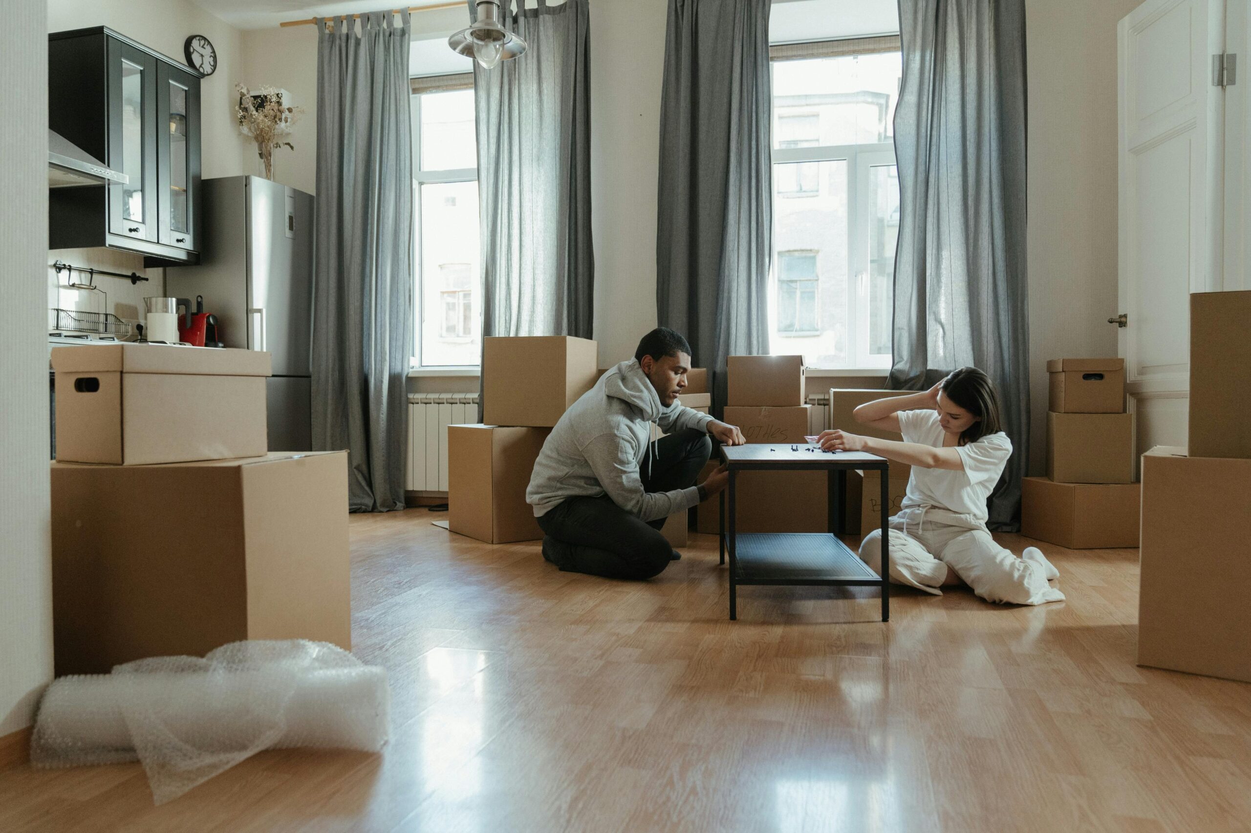 Young couple assembling furniture in their new apartment, surrounded by cardboard boxes.