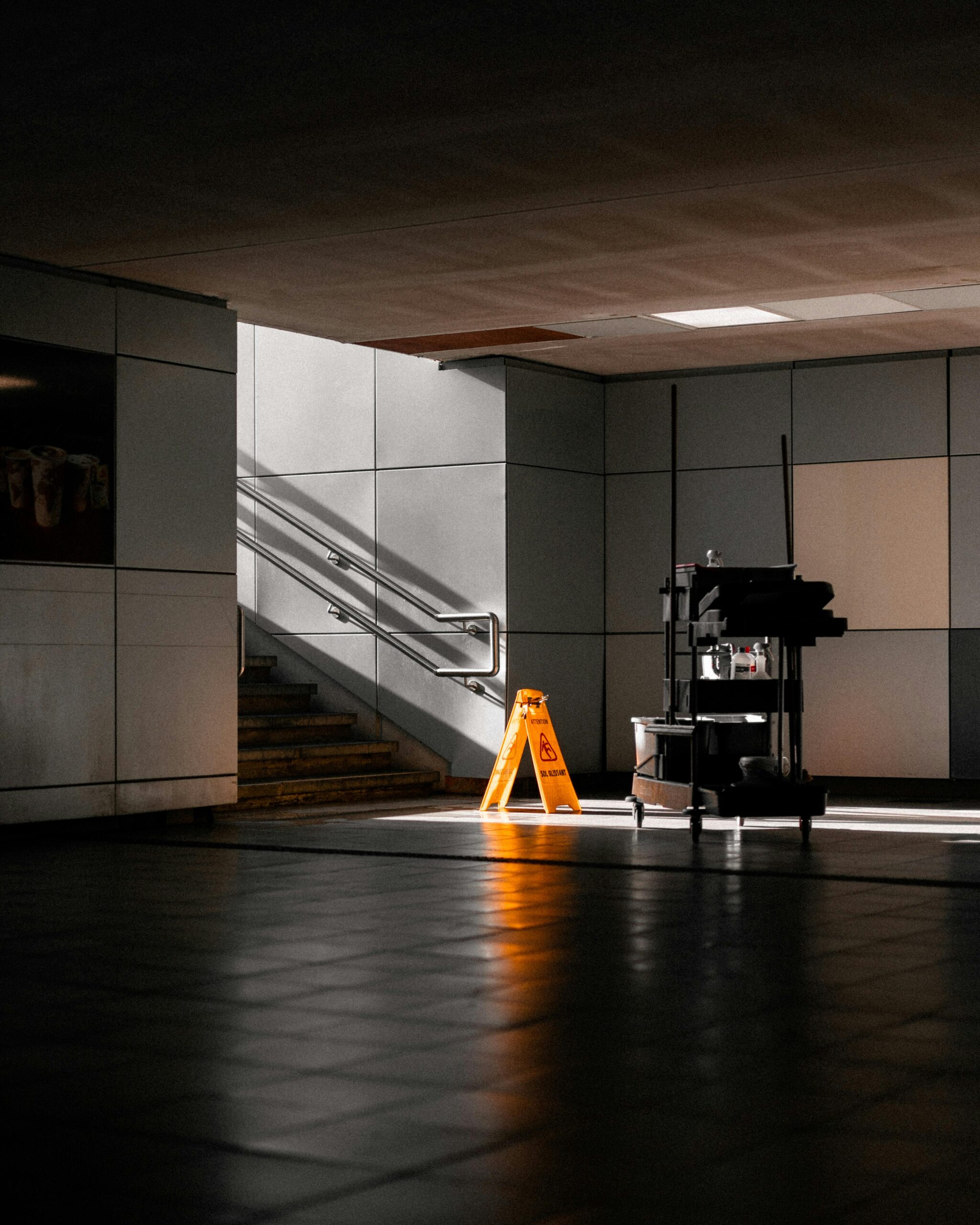 A well-lit underground corridor featuring stairs, cleaning supplies, and warning signs.