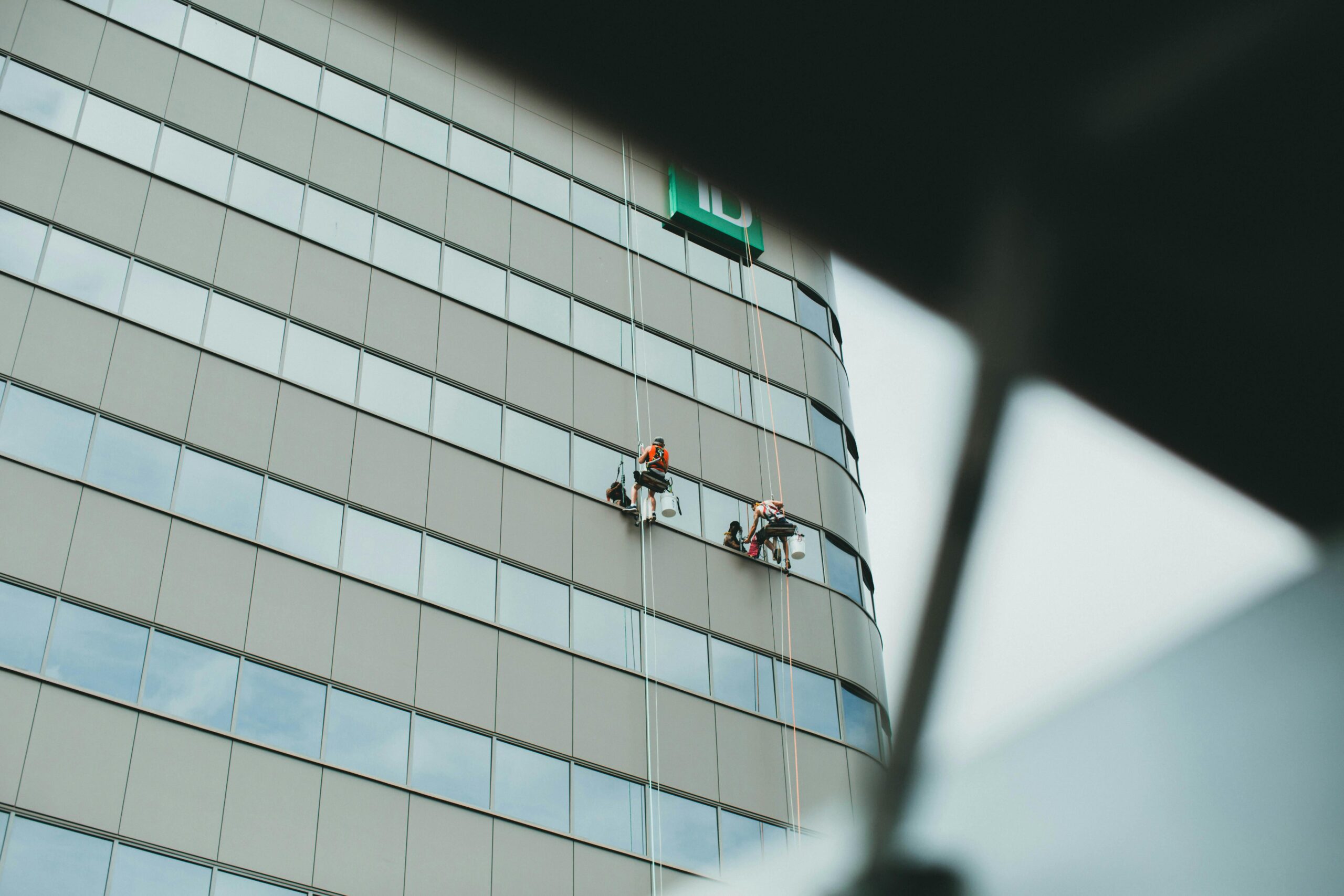 Window cleaners working on the exterior of a tall building, captured from a low angle.